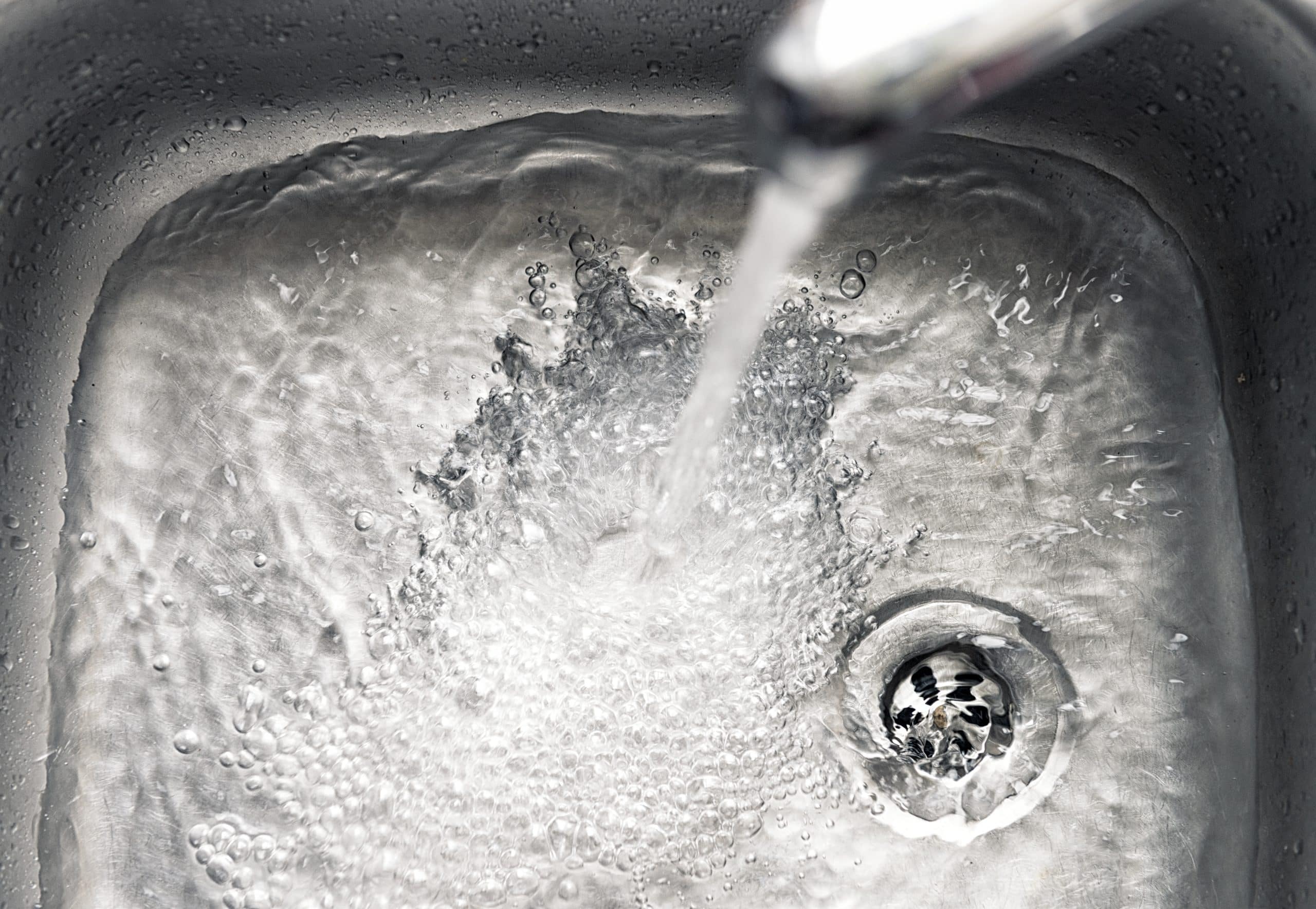 Tap water flowing into a stainless steel sink with a clogged drain