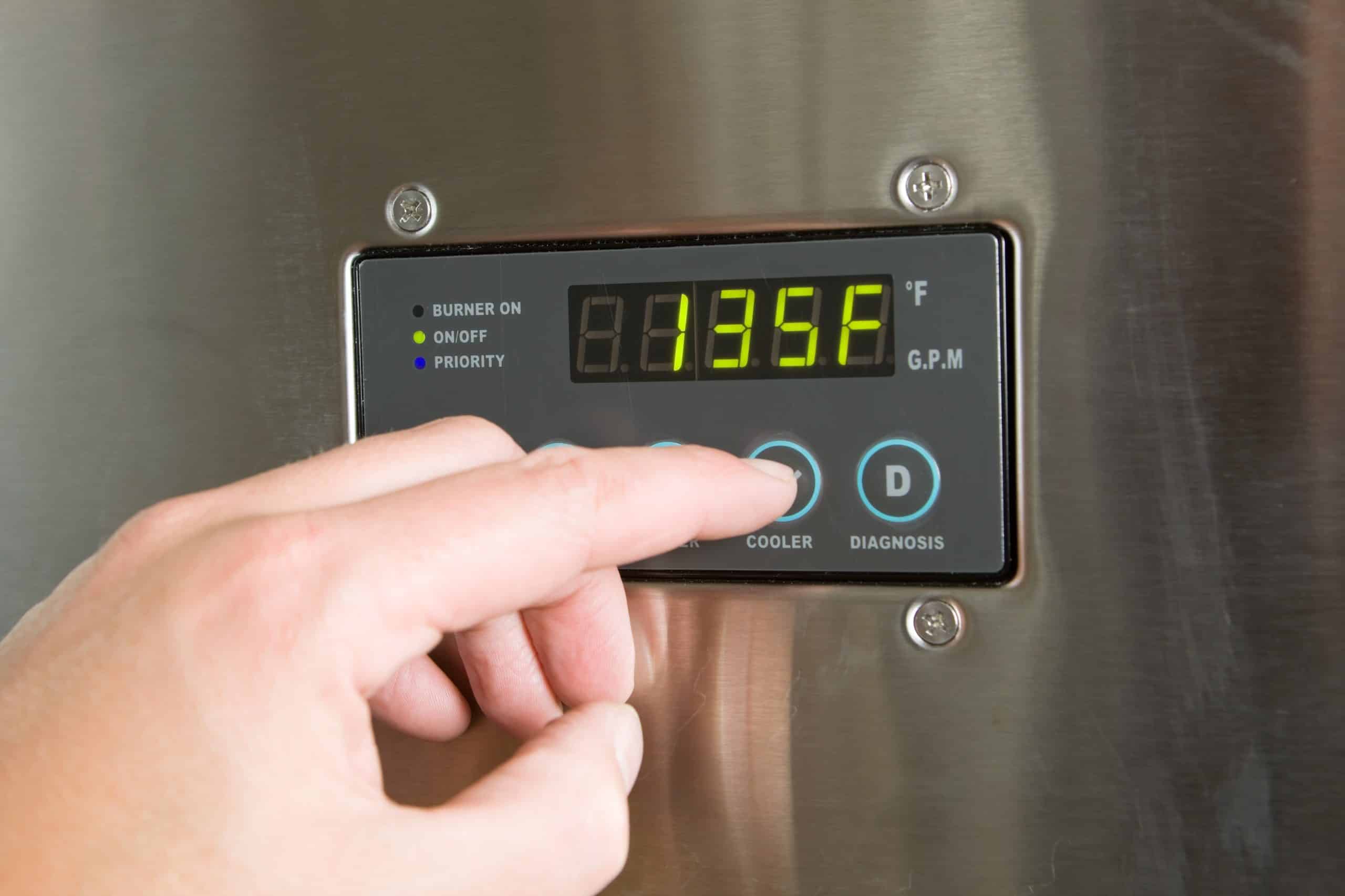 A person’s finger presses a button on the electric control panel of a tankless water heater