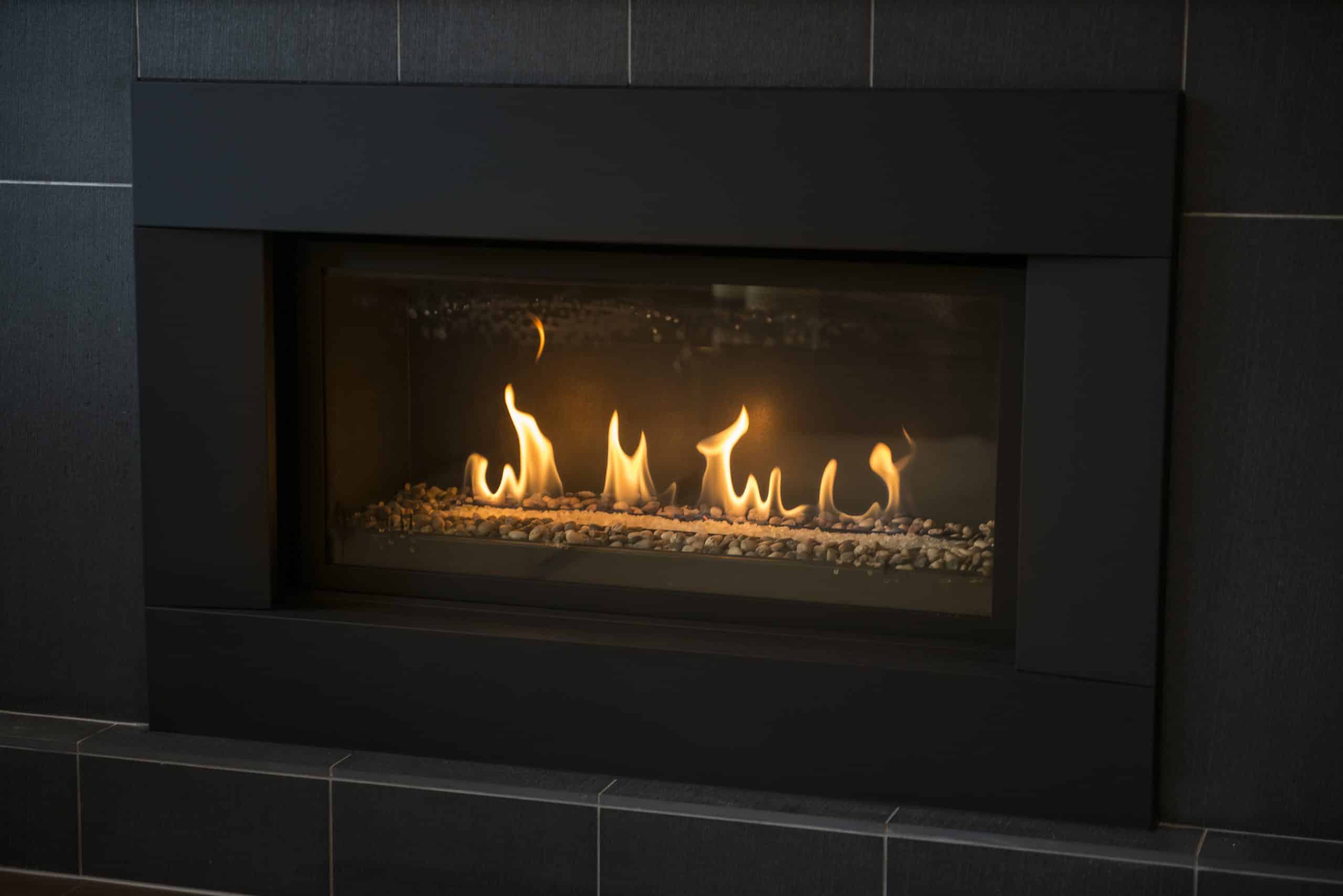 A modern gas fireplace surrounded by a black panel and black tiles