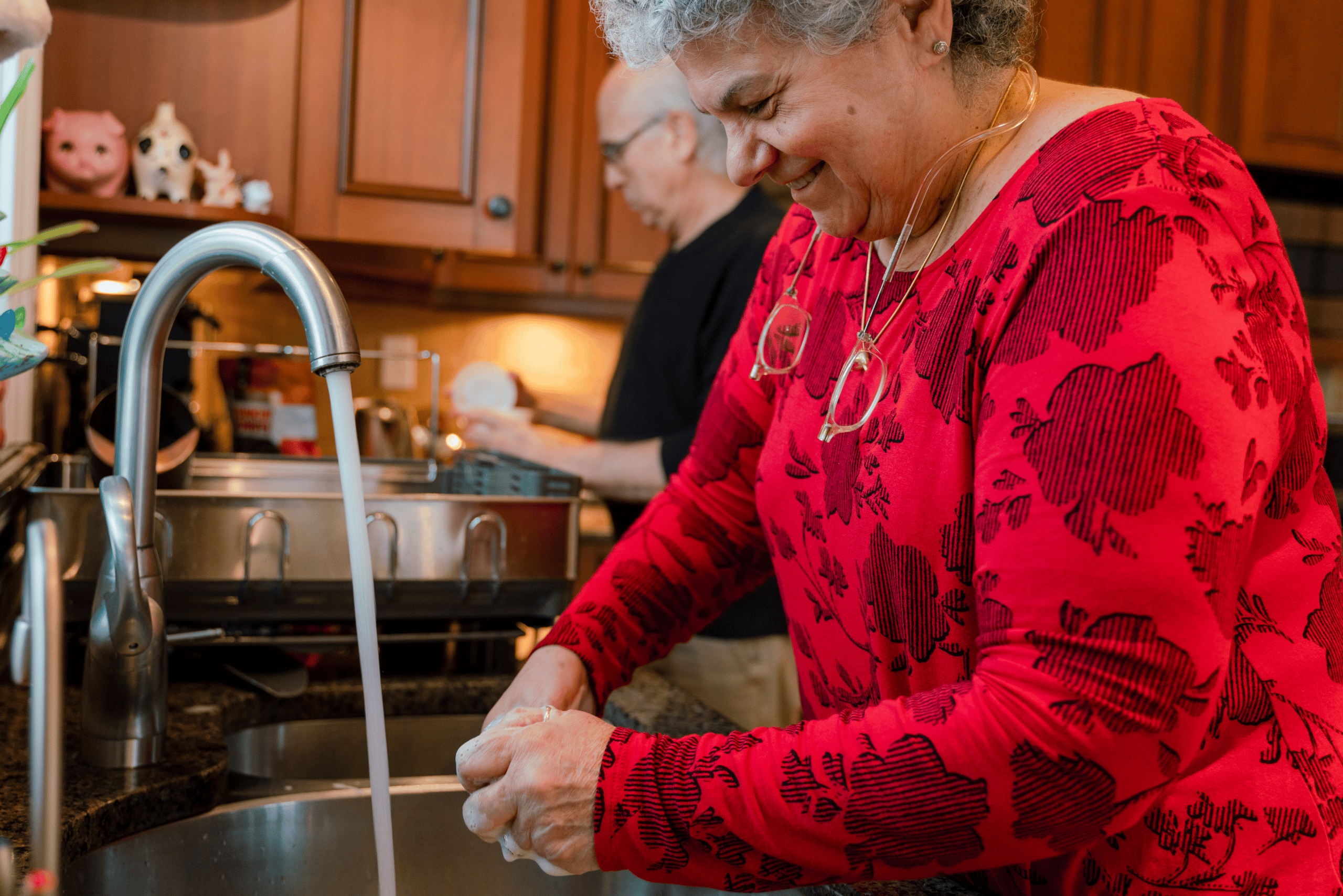 A woman in a festive red blouse washes dishes after a holiday gathering