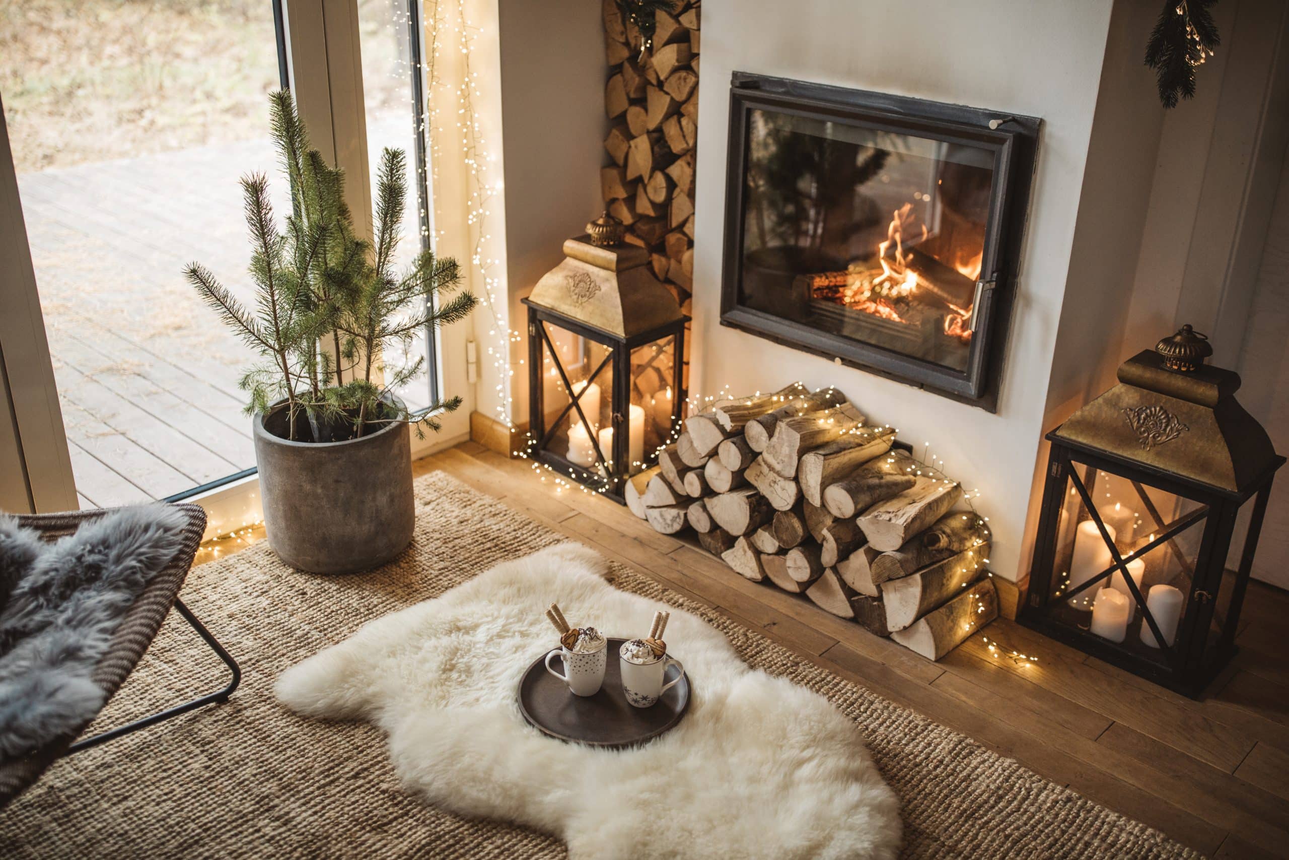 Cozy living room winter interior with gas fireplace, string lights, and mugs of hot chocolate.