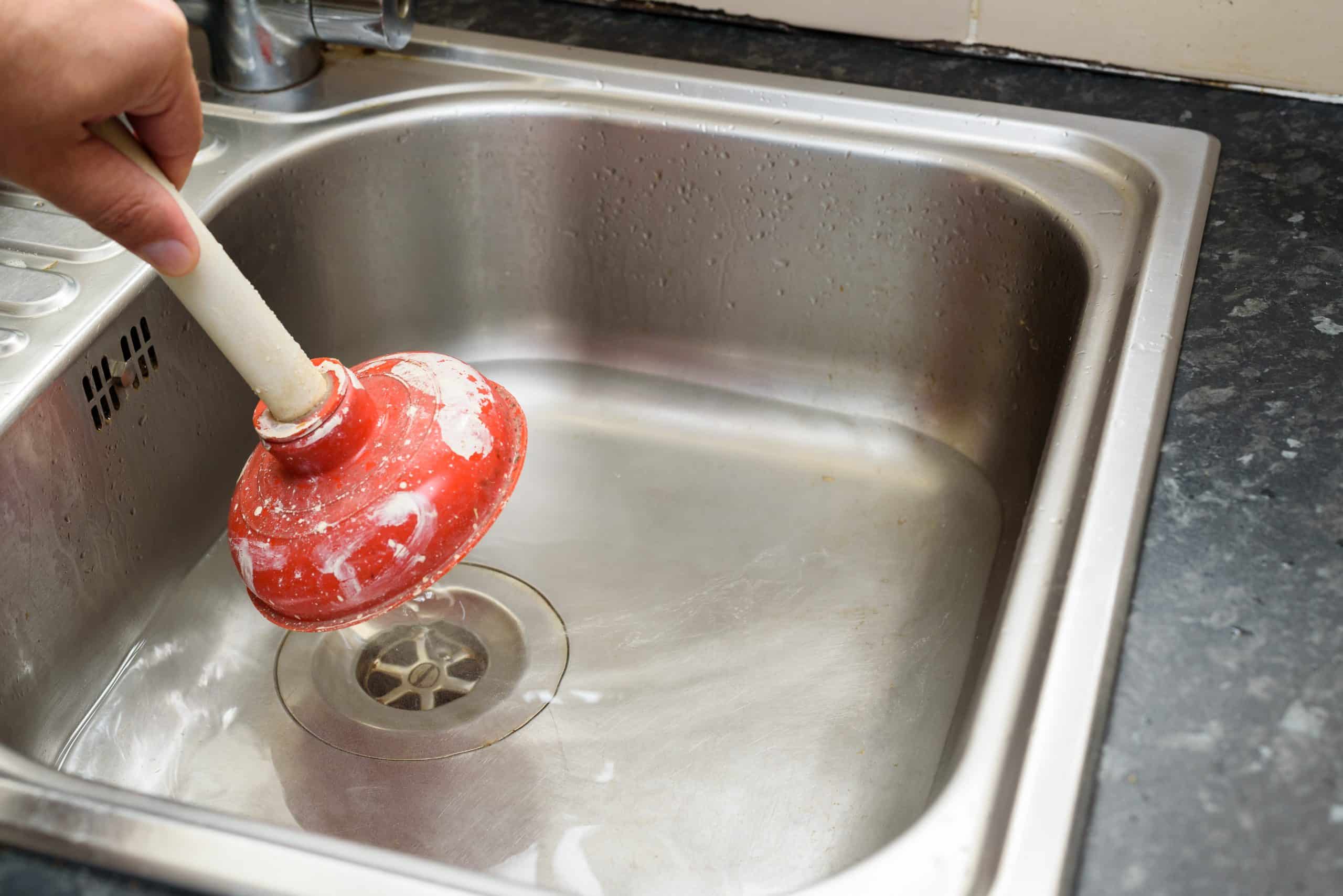 Man using a plunger with one hand to clean a clogged drain in a kitchen sink