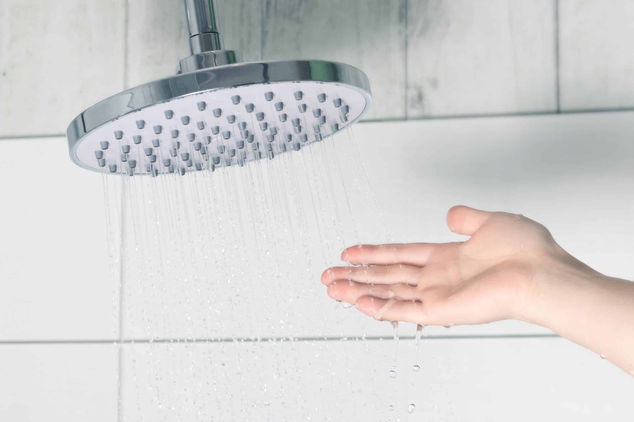 A person’s hand reaching to test the temperature of shower water to see if the water heater is functioning