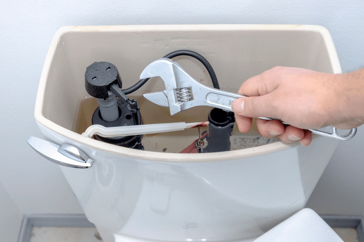 A person holding an adjustable wrench over an open toilet tank to perform toilet repair