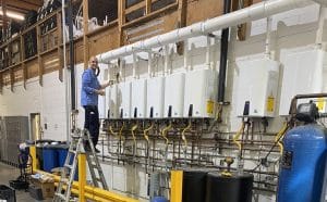 A member of the George Salet Plumbing team installing a bank of tankless water heaters in a local commercial space.