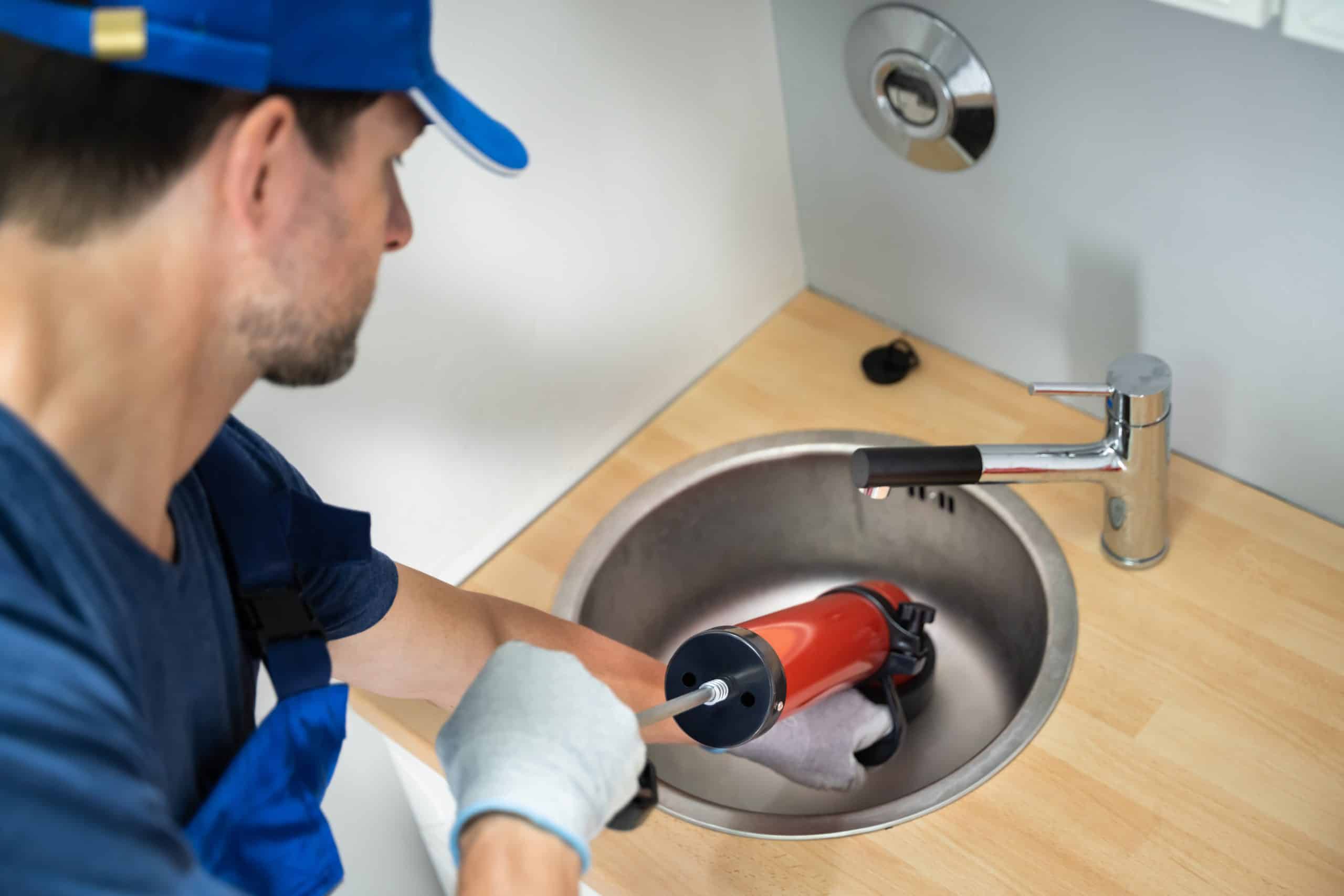 A professional plumber from George Salet wearing a blue uniform cleaning a drain in a San Francisco Home.