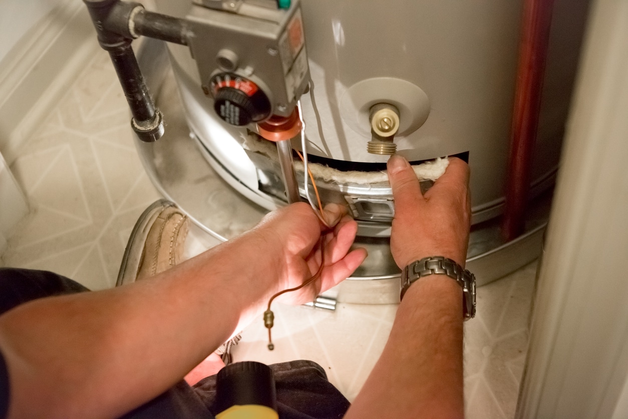An image of someone taking off the access panel of a water heater, with the disconnected thermocouple sticking out