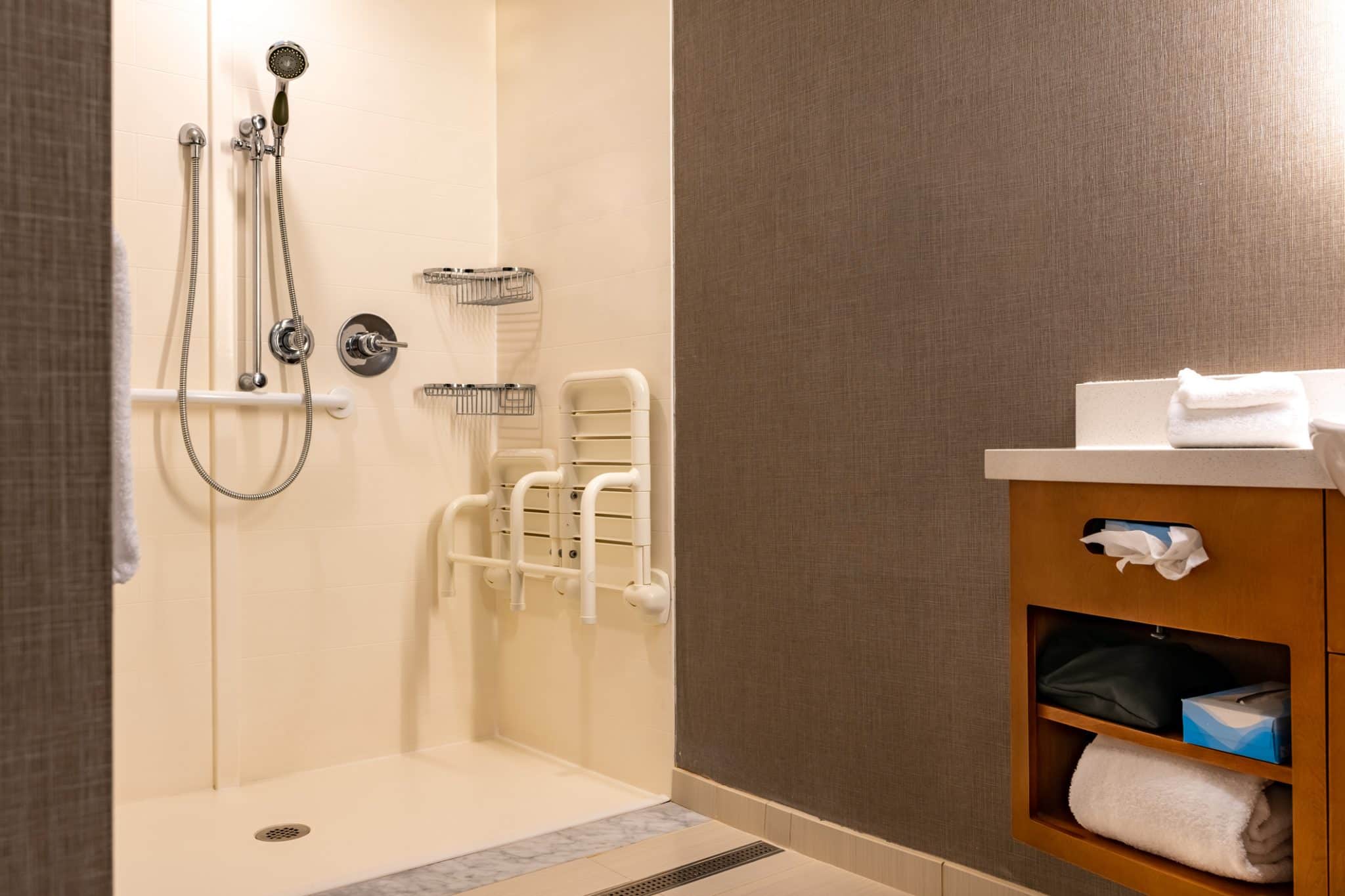 A wheelchair-accessible roll-in shower with grab bars, showing what ADA-compliant bathroom plumbing looks like in practice.