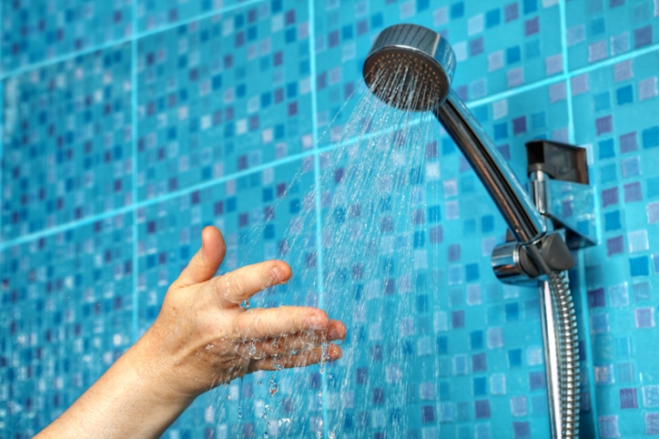 Hand stretching out under the fall of water from the showerhead to check if there is low water pressure in shower.